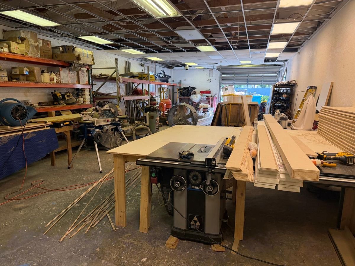 Inside the Visions To Reality workshop with a table saw, lumber and shelving